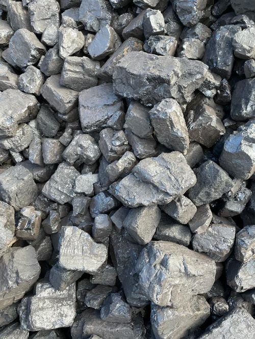 Kupa błyszczącego, czarnego węgla kamiennego o nieregularnych kształtach, oświetlona naturalnym światłem.