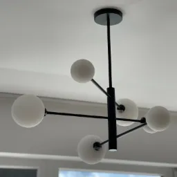 Czarny, nowoczesny żyrandol z mlecznymi kulami zawieszony na białym suficie, widok z dołu, okno w tle.