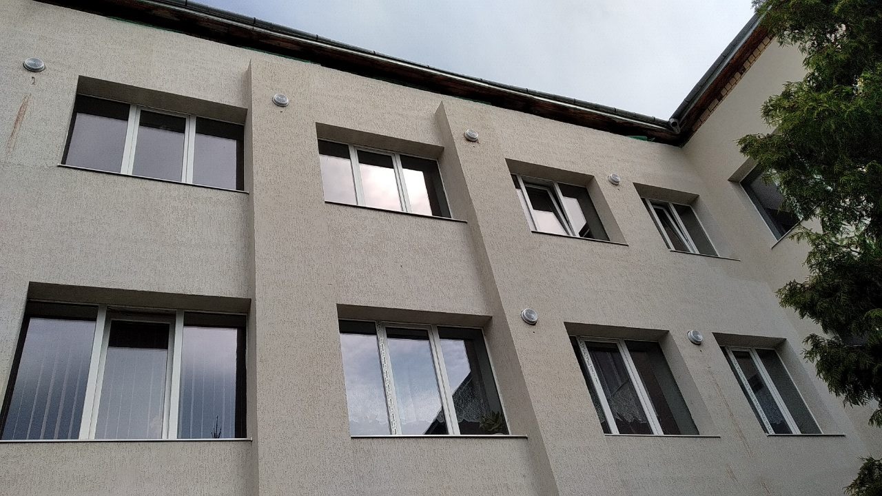 Elewacja budynku z widocznymi oknami i punktowymi lampami na ścianie, ujęcie z dołu pod kątem.