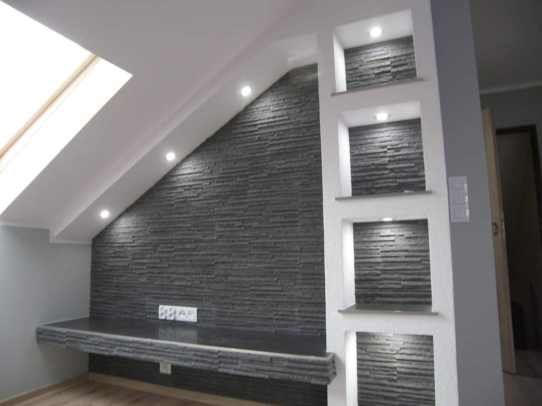 Podświetlona ściana z szarej kamiennej okładziny w pokoju na poddaszu z oknem dachowym i wnękami dekoracyjnymi.
