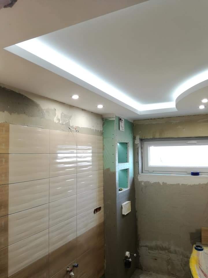 Łazienka w trakcie remontu: położone płytki w odcieniach beżu i brązu, zabudowa z płyty gipsowej z wnękami, sufit podwieszany z oświetleniem LED, ściany w stanie surowym.