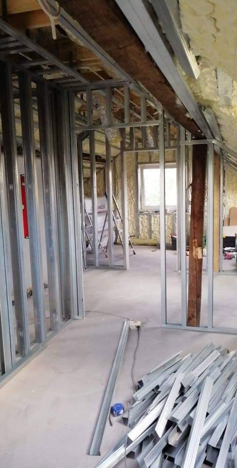 Konstrukcja szkieletowa ścian działowych z profili stalowych, widoczna izolacja wełną mineralną poddasza, pozostałości profili na podłodze, drabina w tle.