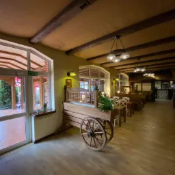 Wnętrze restauracji z drewnianymi wozami-kwietnikami, widok wzdłuż sali z drewnianą podłogą, stropem z belkami i oświetleniem punktowym.