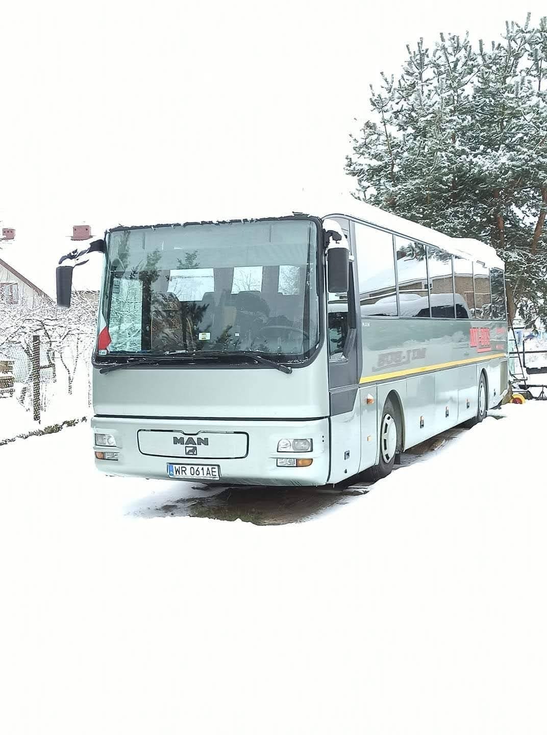 Szary autobus MAN stoi na śniegu w zimowej scenerii, z widocznym numerem rejestracyjnym WR 061AE i drzewem w tle.
