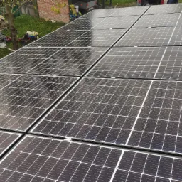 Widok z góry na panele słoneczne na dachu, w tle widoczny fragment ogrodu z zabawkami dziecięcymi i przyczepką.