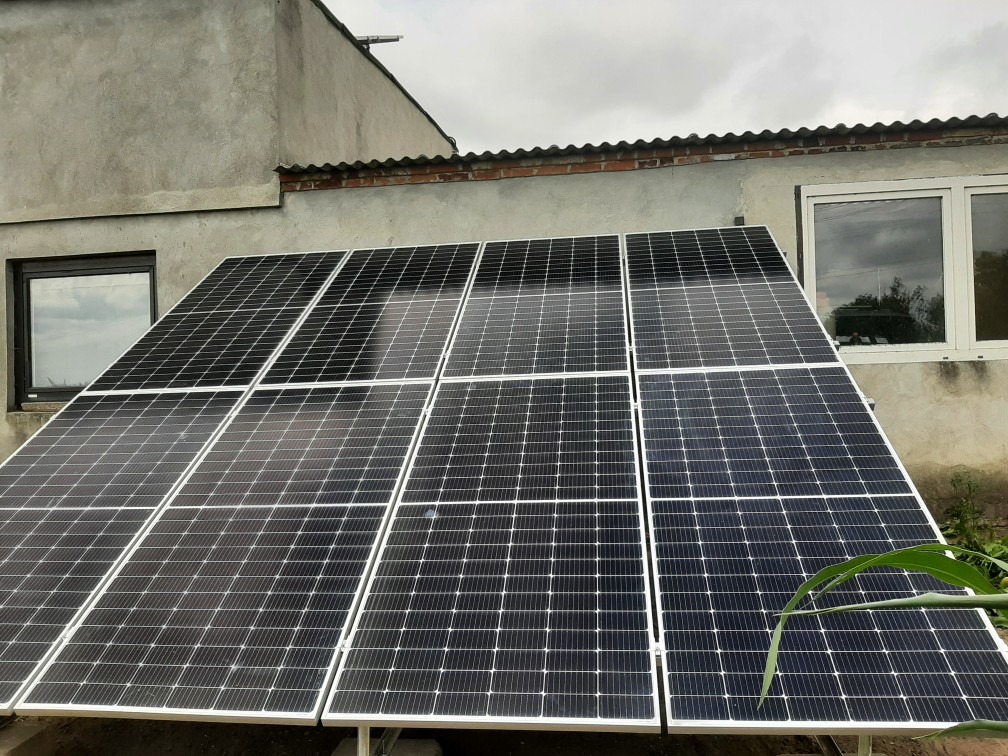 Panel słoneczny zamontowany na dachu budynku gospodarczego z widocznymi dwoma oknami, pochmurne niebo w tle.