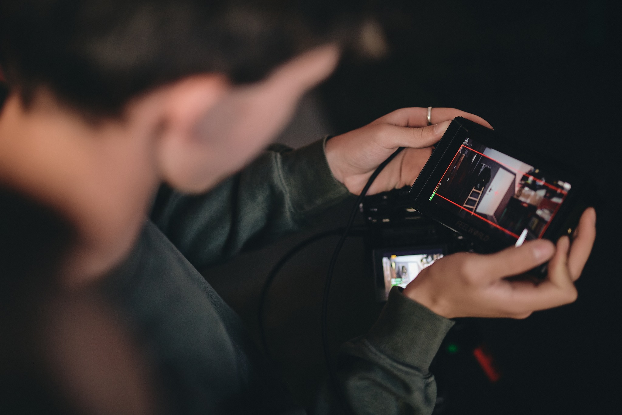 Operator filmowy trzyma monitor podglądowy z widokiem na wnętrze z drabiną, podczas filmowania.