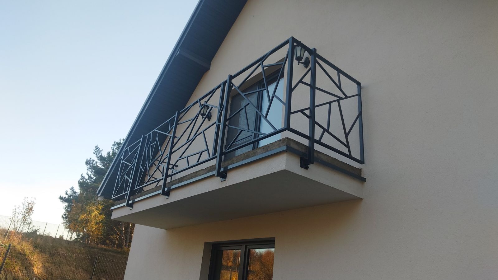 Czarna, geometryczna balustrada balkonowa w Gdyni, z lampami na górze, zamontowana na jasnym budynku, widok z dołu.