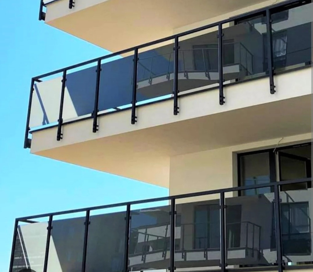Szklane balustrady balkonowe z czarną ramą w nowoczesnym budynku mieszkalnym, uchwycone pod lekkim kątem z dołu.