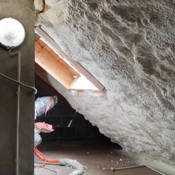 Poddasze ocieplone pianką PUR z widocznym oknem dachowym, lampą i przewodem roboczym na podłodze.