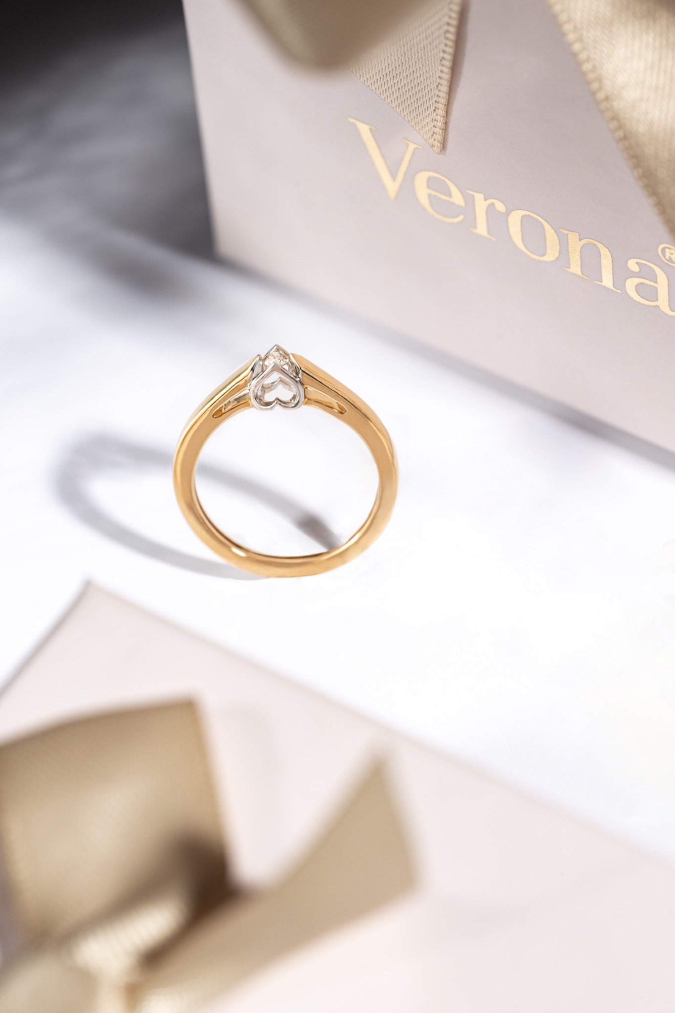 Złoty pierścionek zaręczynowy z diamentem na tle jasnego pudełka prezentowego marki Verona.