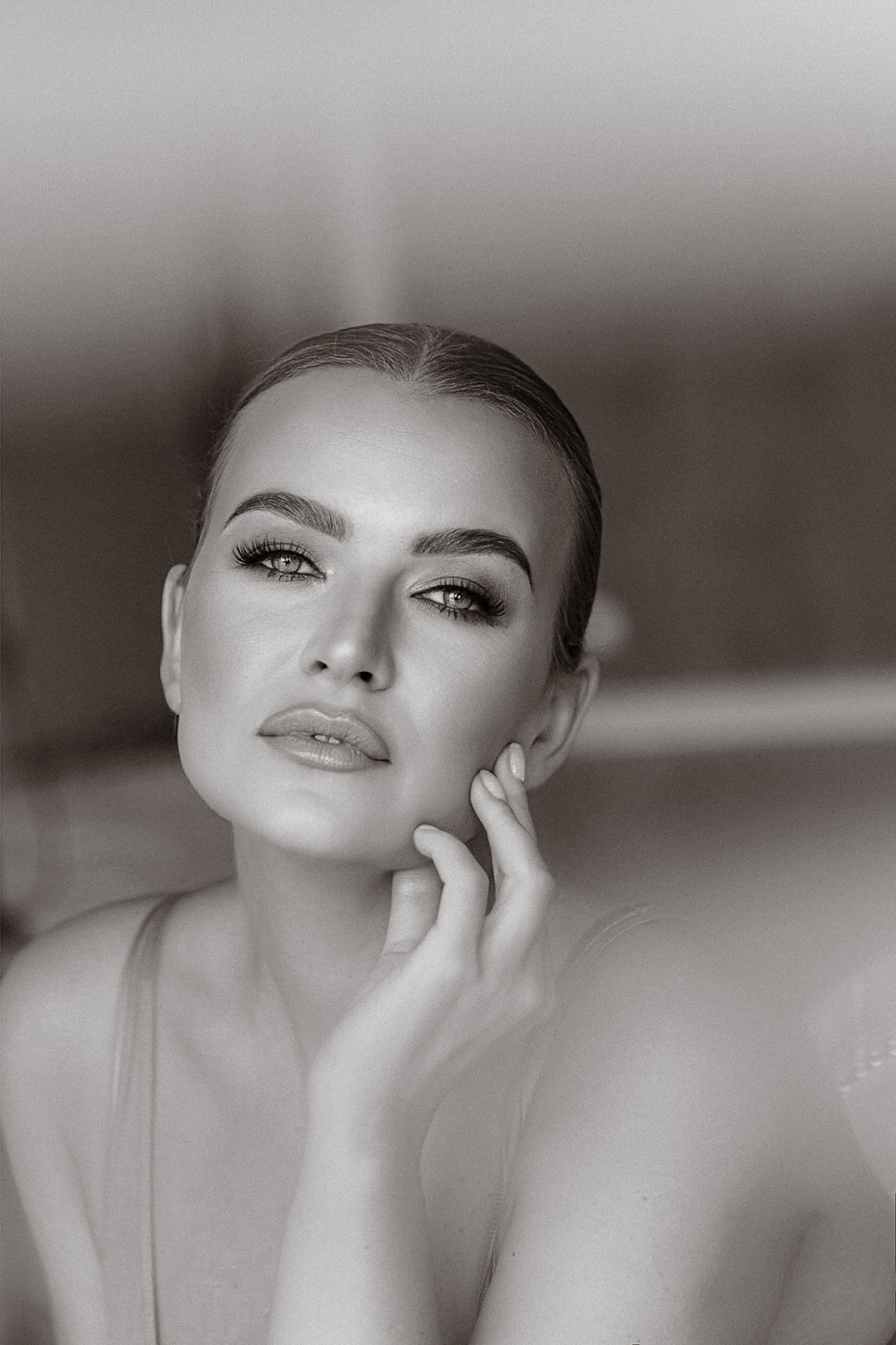 Portret kobiety w czerni i bieli, z dłonią dotykającą policzka, skupiający się na makijażu oczu i ust, z delikatnym, rozmytym tłem.