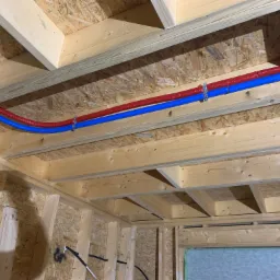 Czerwona i niebieska rura wodna PEX zamocowana do drewnianej konstrukcji stropu w trakcie budowy domu.