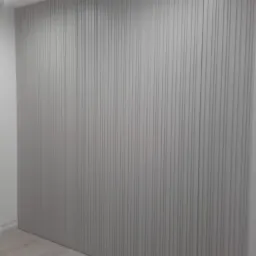 Ściana z szarych paneli pionowych z subtelnymi rowkami, oświetlona górnym światłem, widoczna częściowo podłoga z jasnego drewna.