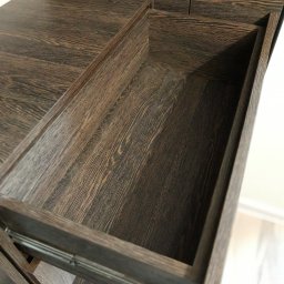 WREM SPÓŁKA Z OGRANICZONĄ ODPOWIEDZIALNOŚCIĄ - Wysunięta szuflada z ciemnego drewna z widoczną strukturą słojów, zamontowana na metalowych prowadnicach. Ujęcie z góry, ukazujące wnętrze szuflady i fragment mebla.