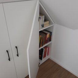 WREM SPÓŁKA Z OGRANICZONĄ ODPOWIEDZIALNOŚCIĄ - Biała szafa wnękowa z czarnymi uchwytami, częściowo otwarta, ukazująca półki z książkami, dopasowana do skosu dachu.