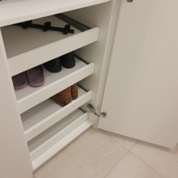 WREM SPÓŁKA Z OGRANICZONĄ ODPOWIEDZIALNOŚCIĄ - Wnętrze białej szafy z wysuwanymi półkami na buty, widoczne buty na półkach, otwarte drzwi szafy z zawiasami.