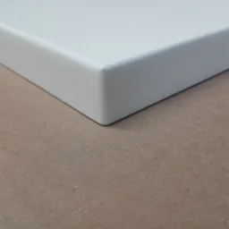 Fragment białego, matowego blatu z zaokrąglonym rogiem na tle beżowej powierzchni.