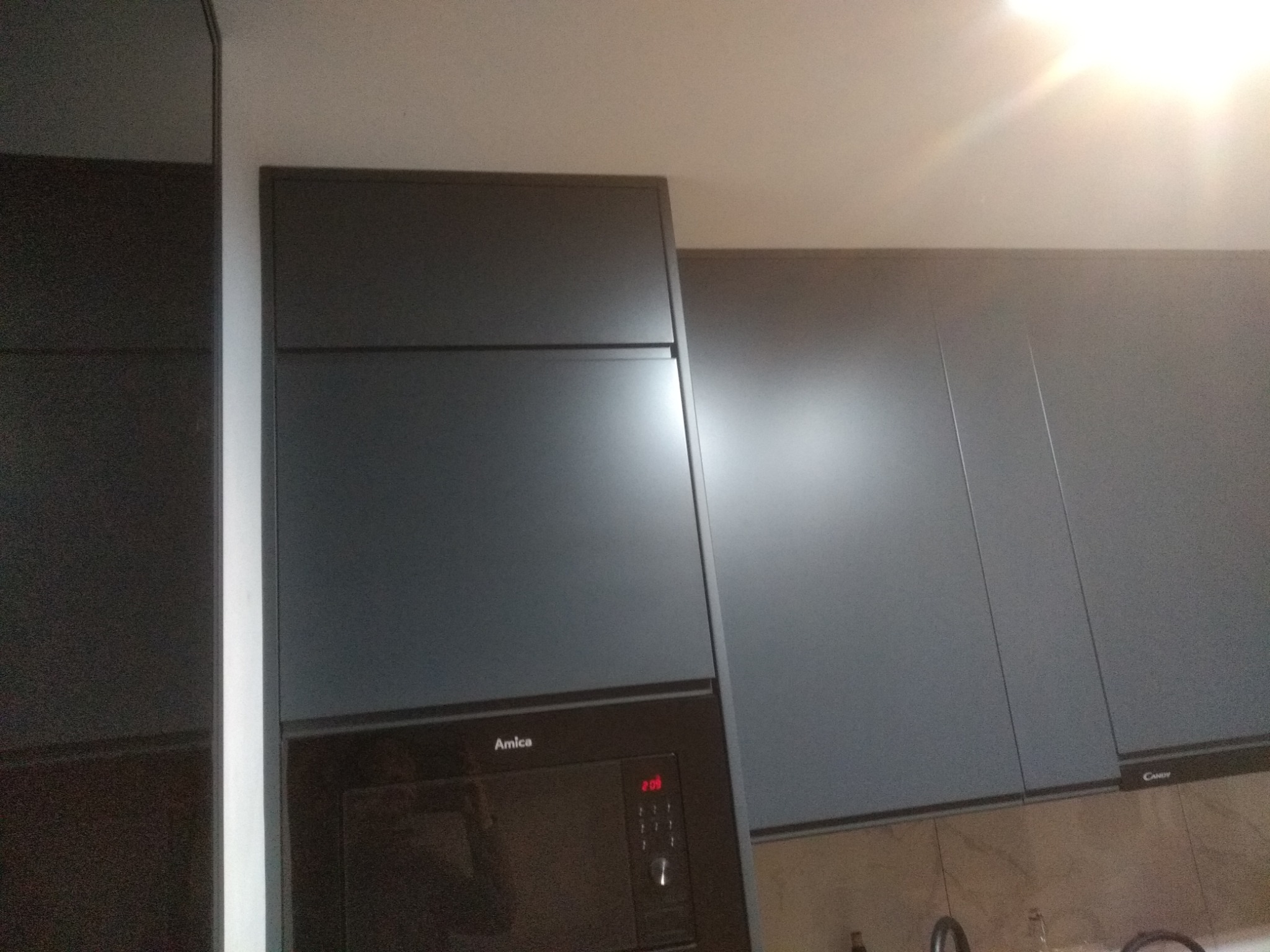 Ciemnoszare szafki kuchenne z piekarnikiem Amica i okapem Candy, minimalistyczny design, oświetlenie sufitowe. Fronty bez uchwytów.