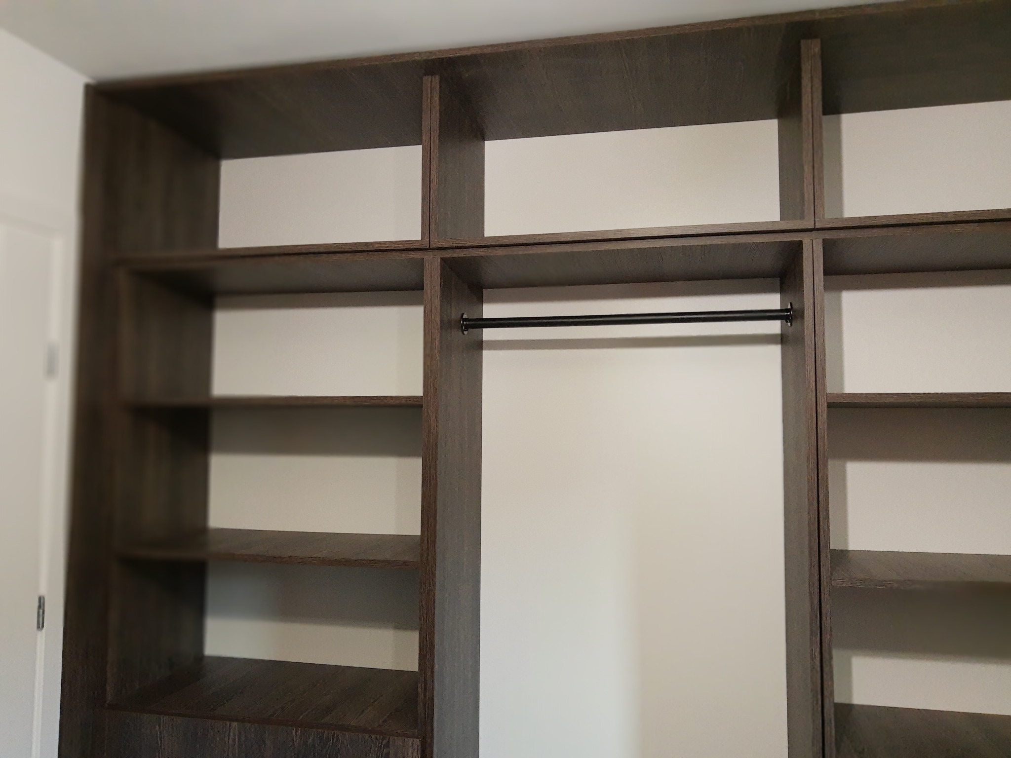 Wnętrze szafy wnękowej z ciemnego drewna, z półkami i drążkiem na ubrania. Widok z dołu, ukazujący strukturę i wykończenie materiału.