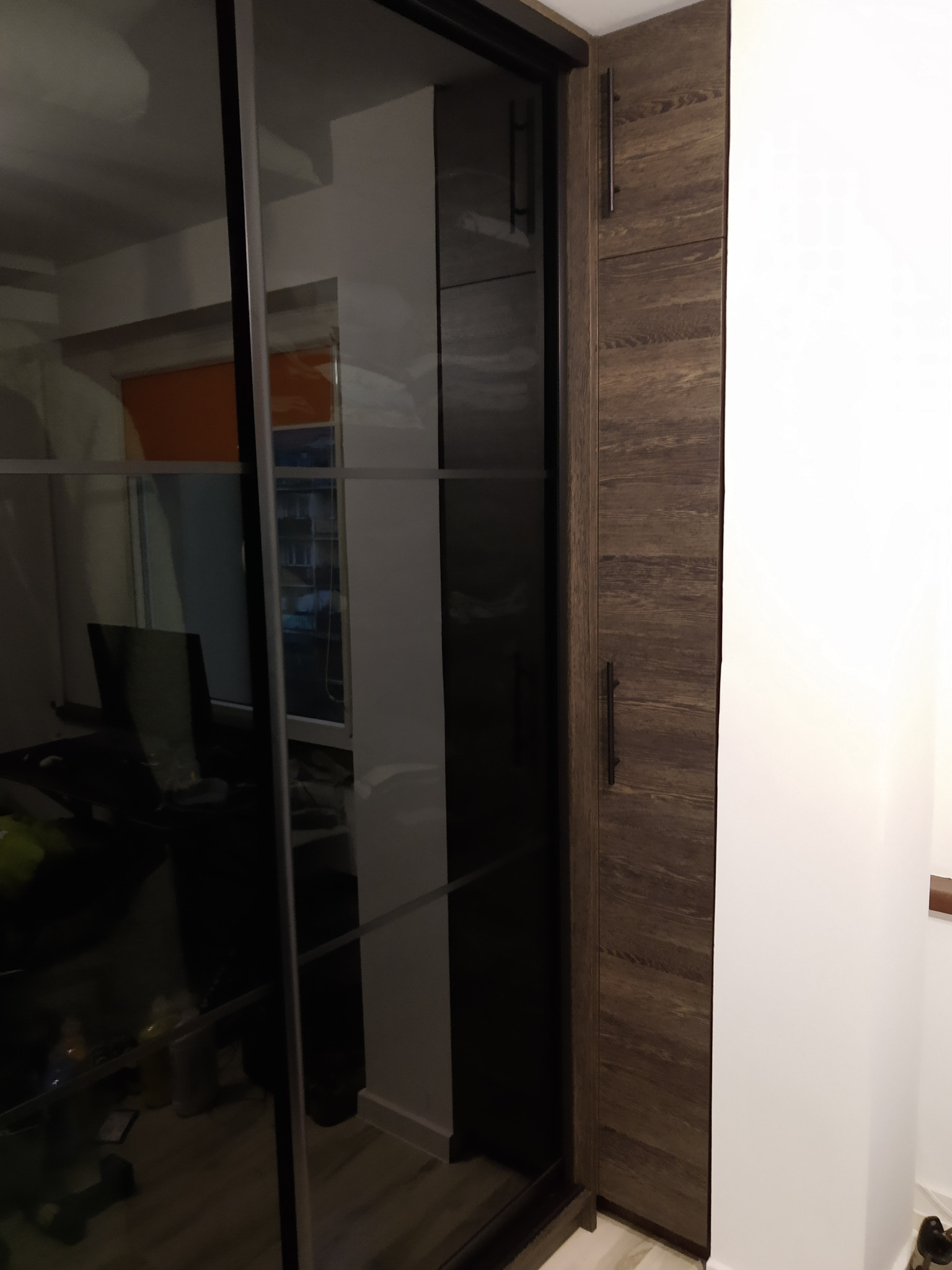 Nowoczesna szafa wnękowa z przesuwnymi, lustrzanymi drzwiami i drewnianymi panelami bocznymi. Widoczne detale wykończenia i uchwyty.