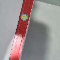 Czerwona poziomica przyłożona do świeżo nałożonego, gładkiego tynku na ścianie, bąbelek w centralnym położeniu.