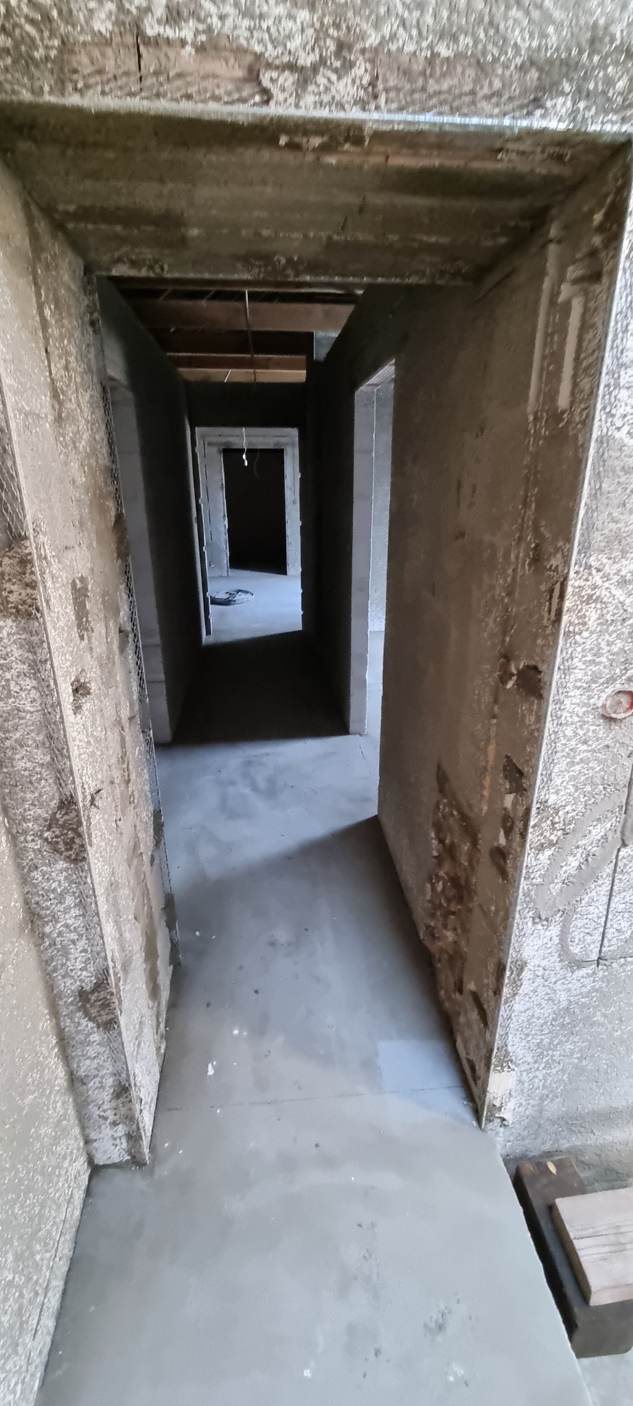 Korytarz w surowym stanie po nałożeniu tynków cementowo-wapiennych, widoczne ślady po łatach na ścianach i siatka podtynkowa na narożach.
