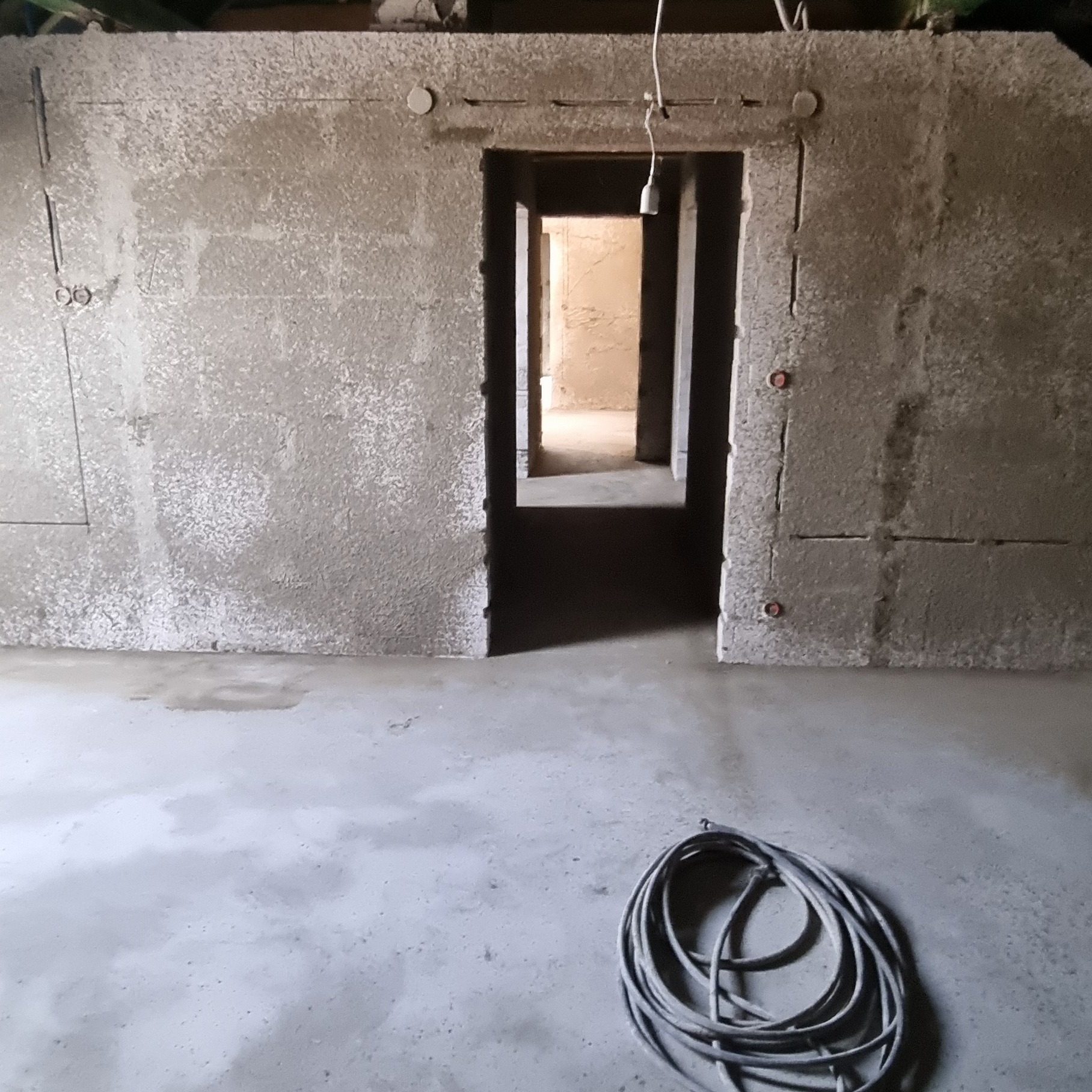 Surowe wnętrze po nałożeniu tynków na ściany z gazobetonu, widoczne instalacje elektryczne i zwój kabla na posadzce.
