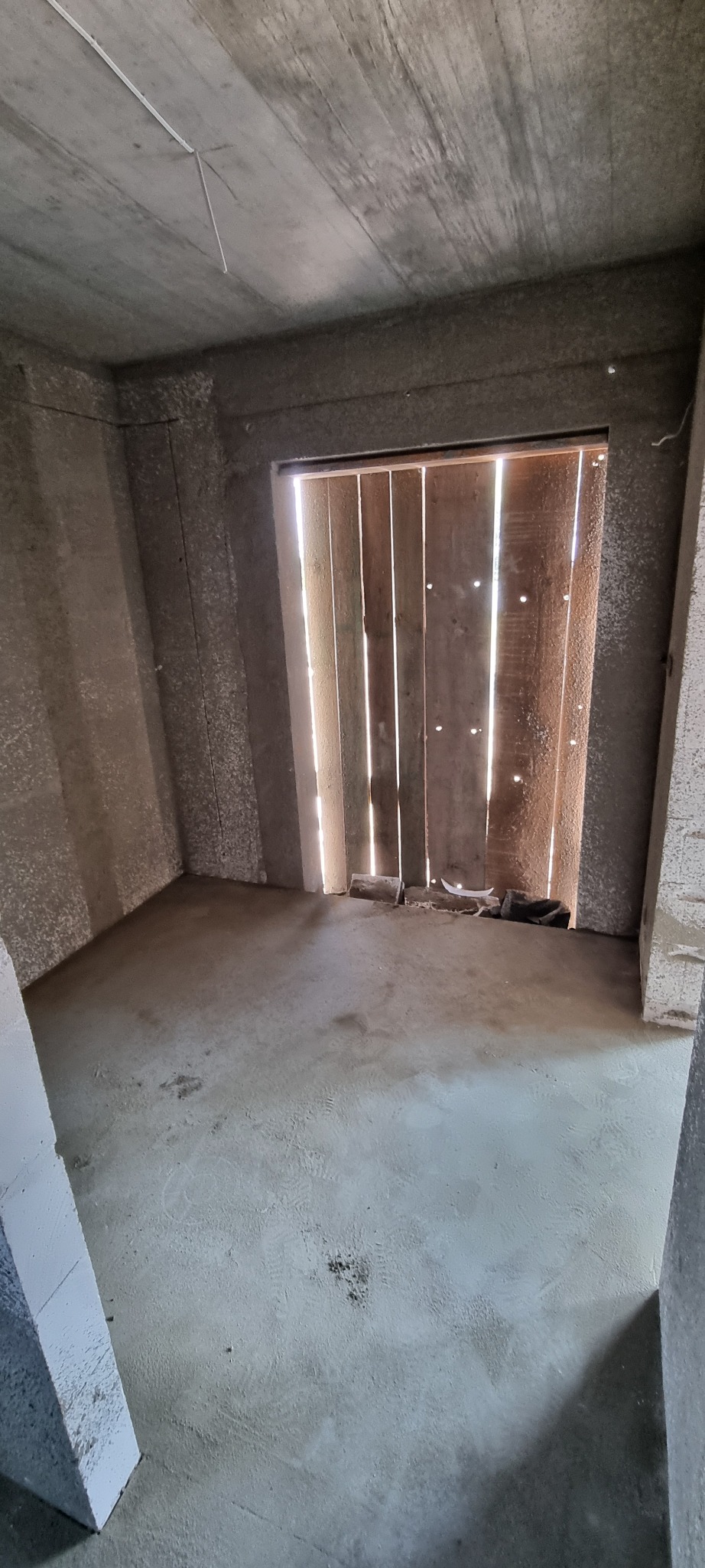 Surowe wnętrze z tynkami maszynowymi na ścianach i suficie, widoczne ślady po pracach i drewniane szalunki okienne przepuszczające światło dzienne.