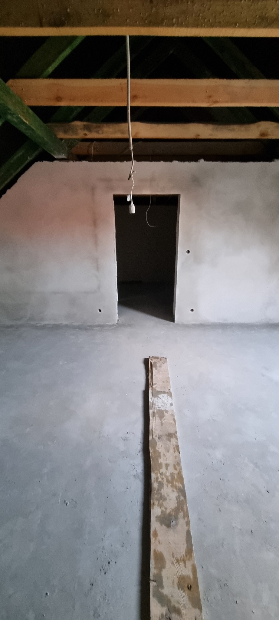 Świeżo położone, szare tynki na poddaszu, widoczne drewniane krokwie i deska na podłodze.