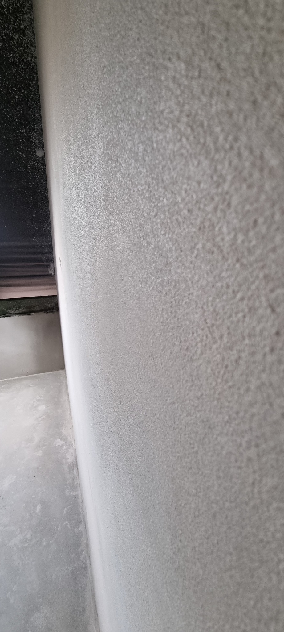 Świeżo nałożony, jasny tynk maszynowy na ścianie wewnętrznej, widoczna faktura i gładkie wykończenie narożnika.