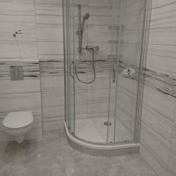 Konkretna Ekipa Remontowa - Nowoczesna łazienka wykończona w szaro-białej kolorystyce, z kabiną prysznicową z zaokrąglonymi drzwiami, wiszącą toaletą i płytkami imitującymi marmur na ścianach, oraz dużymi płytkami podłogowymi.