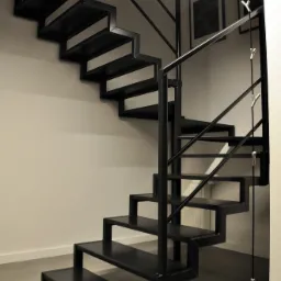 Nowoczesne, czarne schody metalowe z minimalistyczną balustradą w jasnym wnętrzu, oświetlone listwą LED, z widocznymi elementami dekoracyjnymi na ścianie.