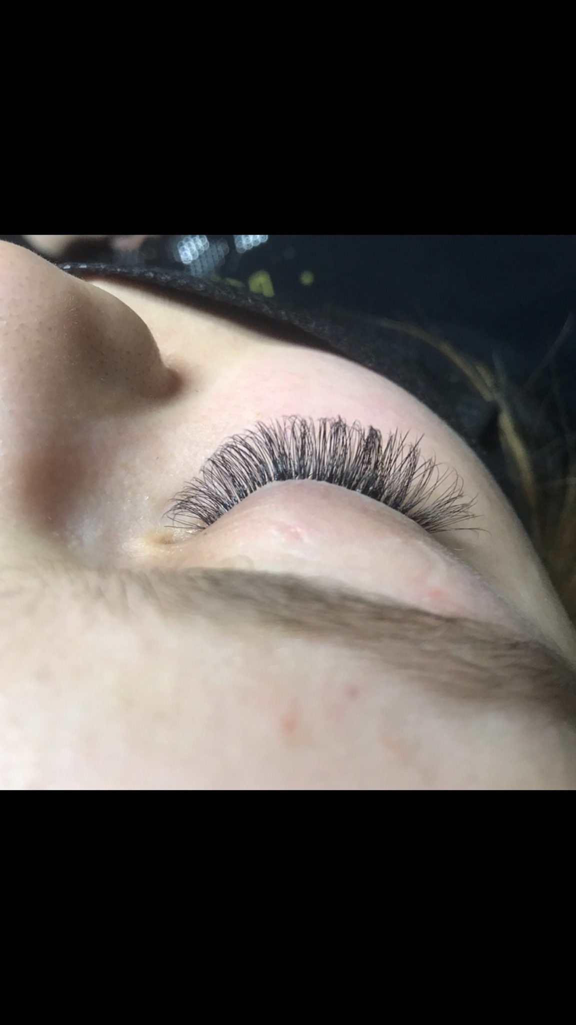 Zbliżenie na oko z gęstymi, czarnymi, profesjonalnie przedłużonymi rzęsami w stylu 'kocie oko', widoczna delikatna skóra powiek.