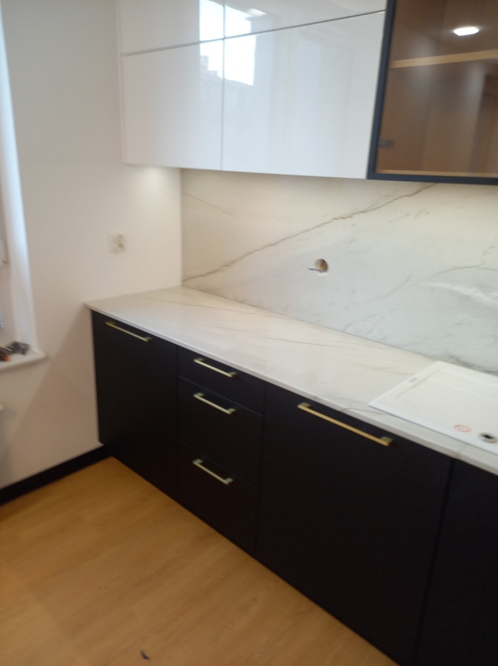 Nowoczesna kuchnia z czarnymi szafkami i blatem imitującym marmur, złote uchwyty, białe szafki wiszące.