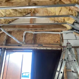 Montaż sufitu podwieszanego z izolacją z wełny mineralnej, widoczne profile metalowe, przewody w peszlach oraz drabina aluminiowa.