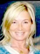 Portret uśmiechniętej kobiety z blond włosami, patrzącej wprost, z delikatnym makijażem i subtelną biżuterią na szyi, na rozmytym niebieskim tle.