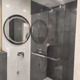 RS Concept Rafał Szlendak - Nowoczesna łazienka z okrągłym lustrem z podświetleniem LED, szklaną kabiną prysznicową z deszczownicą i baterią podtynkową na ścianie wyłożonej jasnymi i ciemnymi płytkami.