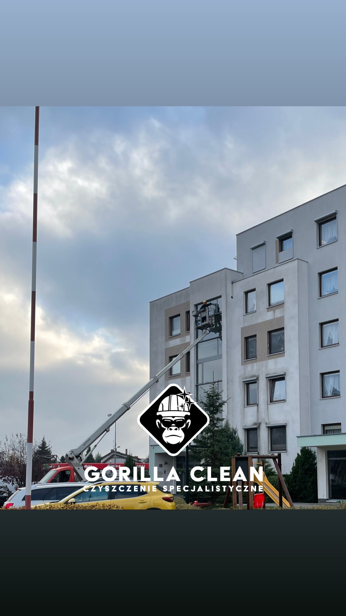 Pracownik na podnośniku koszowym czyści okna wysokiego budynku mieszkalnego, logo firmy Gorilla Clean w dolnej części kadru.