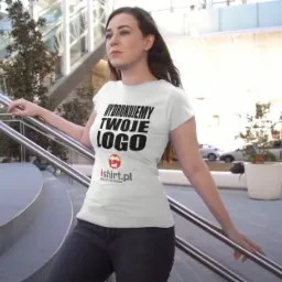 Kobieta pozuje na schodach w białej koszulce z czarnym nadrukiem 'Wydrukujemy Twoje Logo' i logo ishir.pl, w tle nowoczesny budynek.