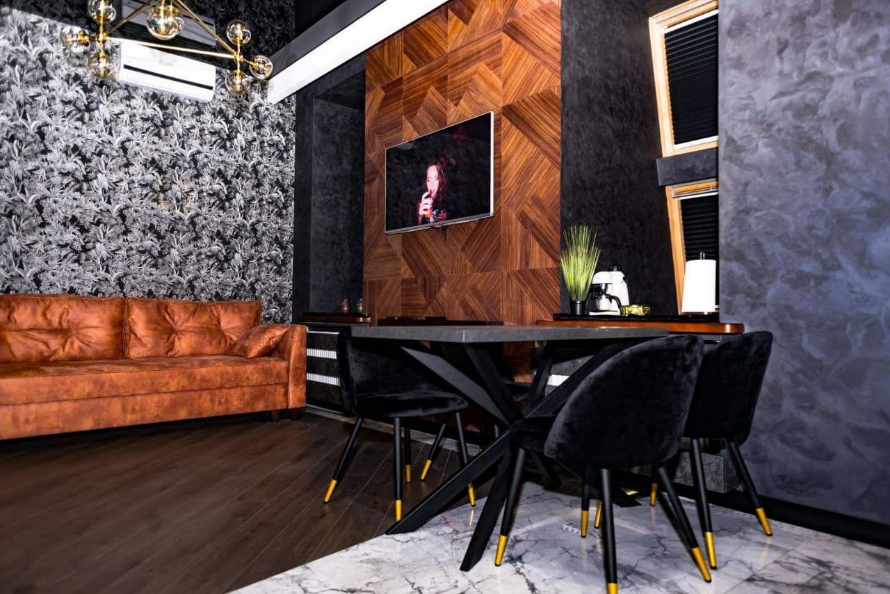 Nowoczesne wnętrze z brązową skórzaną sofą, geometryczną drewnianą ścianą z telewizorem, czarnymi krzesłami z metalowymi nogami, marmurową podłogą i wzorzystą tapetą.