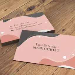 Stos wizytówek z minimalistycznym, różowo-szarym designem i danymi kontaktowymi na drewnianym stole.