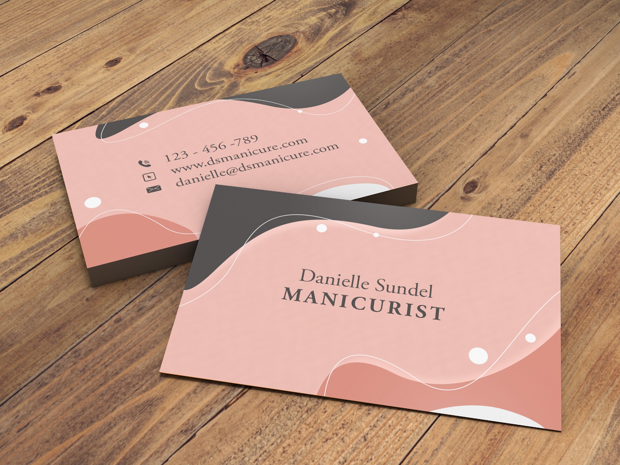 Stos wizytówek z minimalistycznym, różowo-szarym designem i danymi kontaktowymi na drewnianym stole.