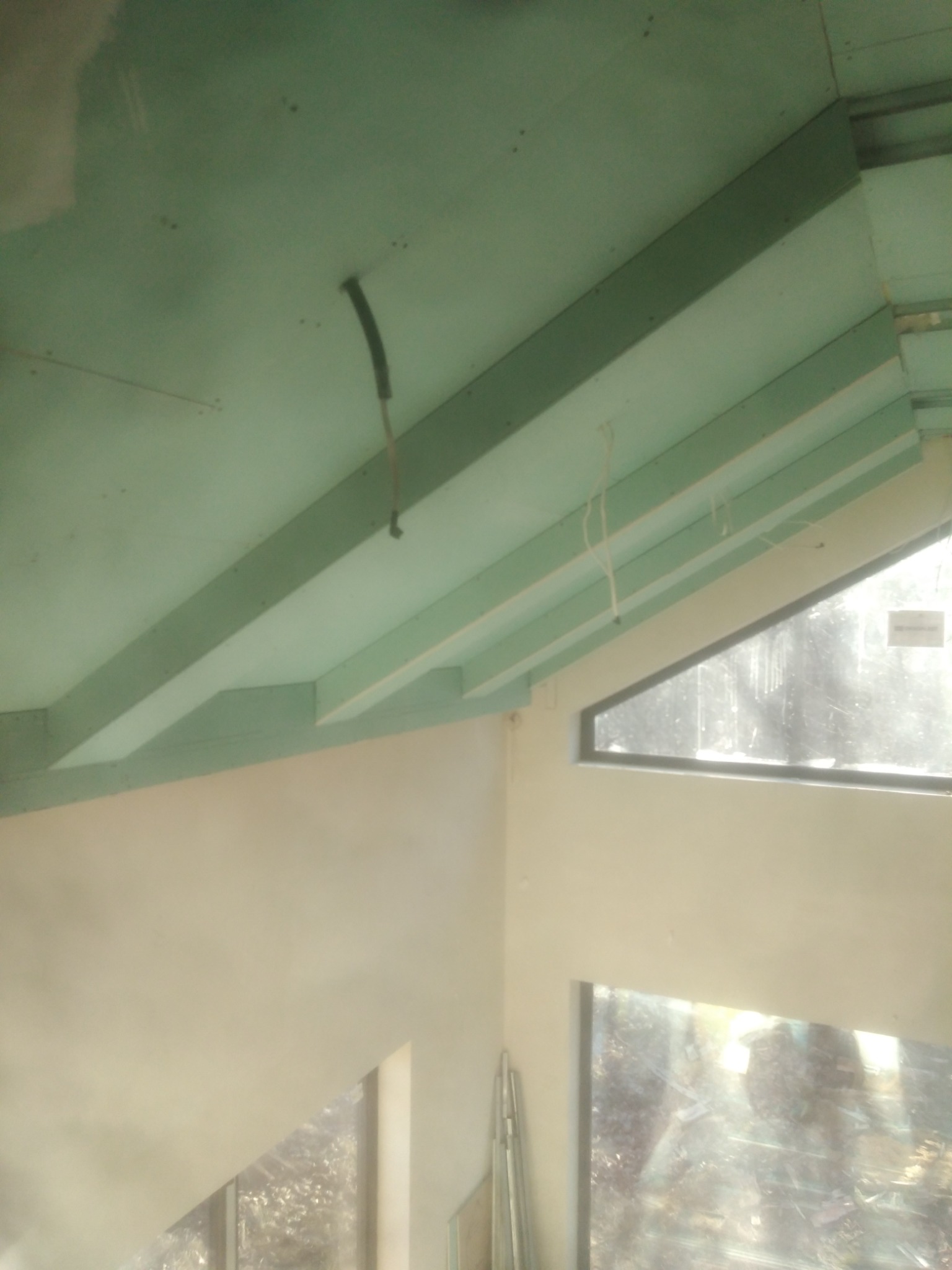 Skośny sufit z zamontowaną zieloną płytą, widoczne profile konstrukcyjne, okno trójkątne i pionowe okno, częściowo zagruntowane ściany.