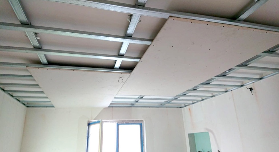 Montaż sufitu podwieszanego: metalowa konstrukcja nośna i częściowo zamontowane płyty gipsowo-kartonowe, widoczne przewody elektryczne.