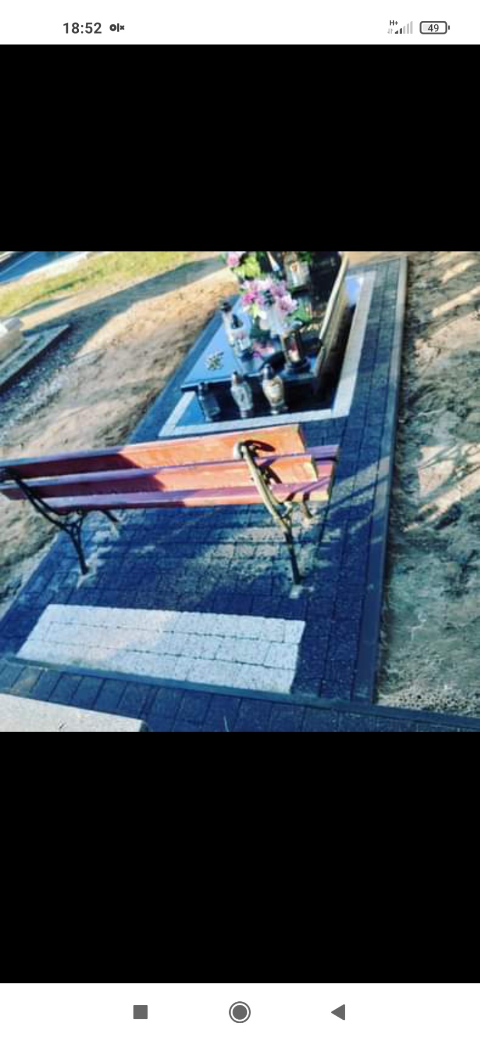 Wykończone miejsce pochówku z ławką i obramowaniem z ciemnej kostki, z jasnym pasem kostki na środku, otoczone piaskiem.