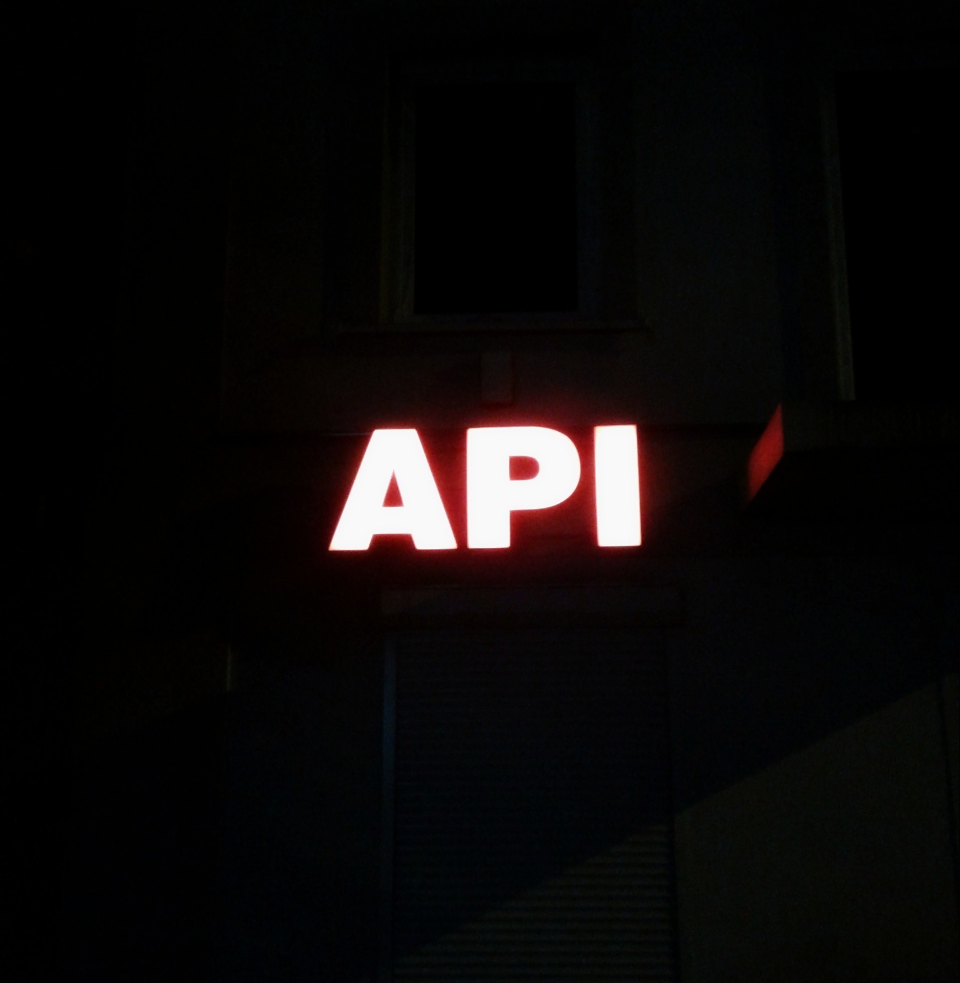 Neonowy napis 'API' na ciemnym tle budynku, widoczny nocą.