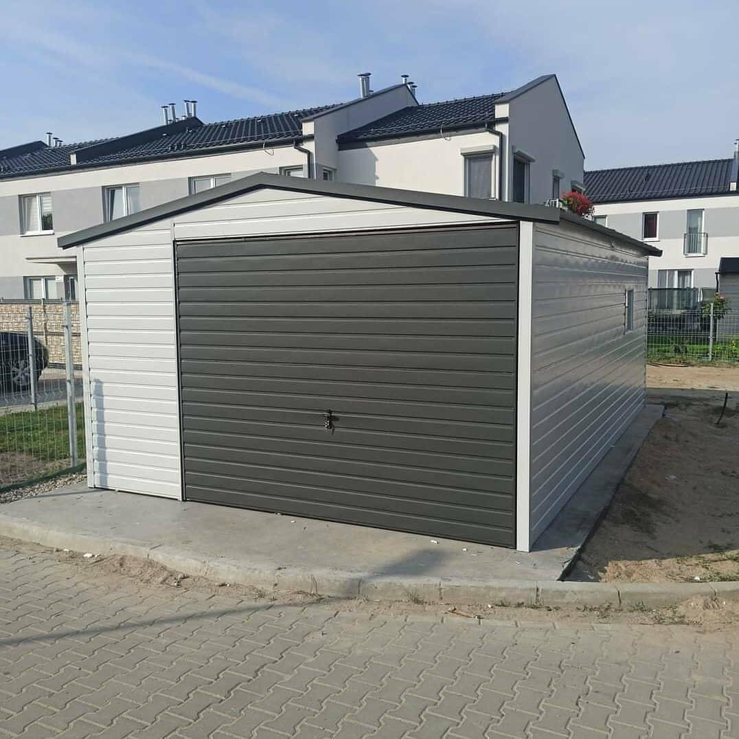 Gotowy, blaszany garaż z szarą bramą segmentową, ustawiony na betonowej wylewce, na tle zabudowy szeregowej.