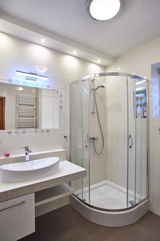 Nowoczesna łazienka z kabiną prysznicową z zaokrąglonym szkłem, umywalką nablatową na blacie z mozaiką i podświetlanym lustrem z dekoracyjnymi okręgami.