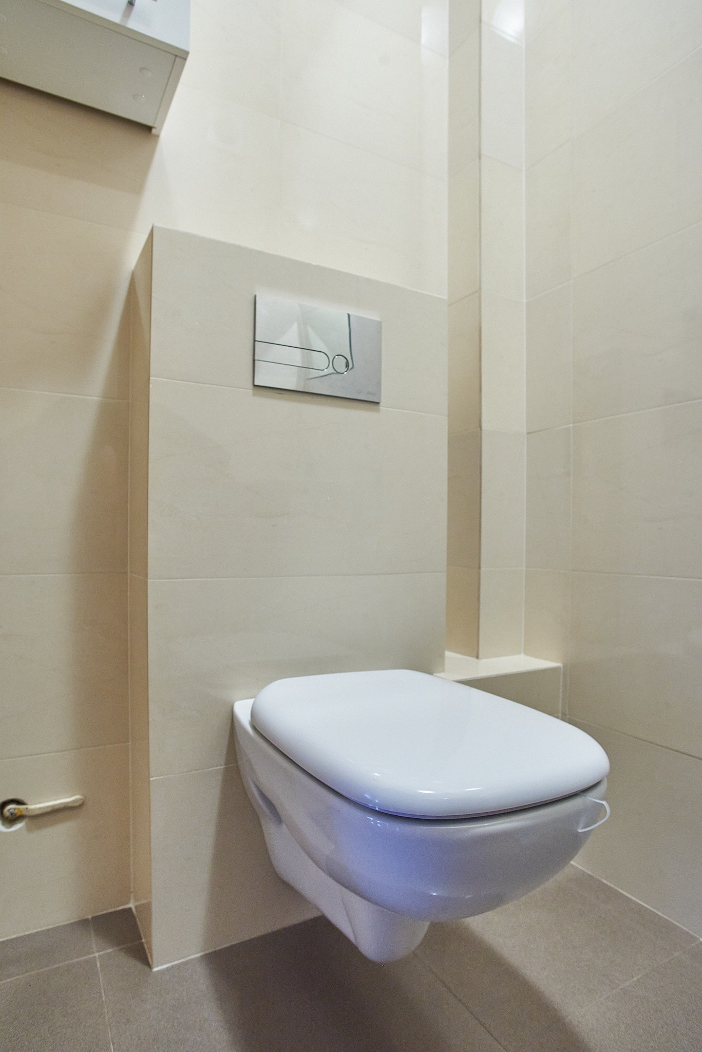 Podwieszana toaleta z chromowanym przyciskiem spłukiwania w łazience wykończonej beżowymi płytkami, Wołomin.